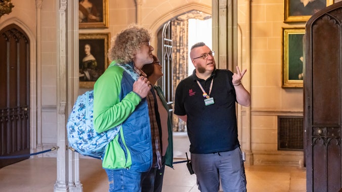 Gwirfoddolwr yn siarad gydag ymwelwyr, yn dangos rhywbeth ar y wal